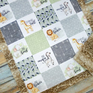 May include: A patchwork baby blanket with animal illustrations and motivational phrases. The blanket has a soft, faux fur trim. Animals include a lion, giraffe, elephant, and zebra. Phrases include "Be Brave", "Be Kind", and "Be Unique".