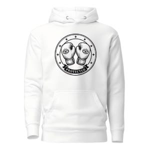 May include: A white hooded sweatshirt featuring a black graphic print on the chest. The design shows two boxing gloves with eyes on them, enclosed in a circular frame with stars and the word PROTECTED printed on a banner at the bottom.