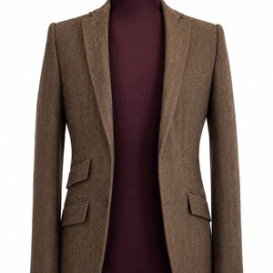 Puede incluir: Un blazer marrón con diseño de espiga exhibido en un maniquí. El blazer tiene dos bolsillos delanteros y solapas con muescas. El torso del maniquí es de color burdeos oscuro, sobre un fondo blanco.