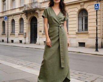 May include: An olive green wrap dress with short sleeves and a matching waist tie. The dress has a V-neckline and a flowing skirt. The model is wearing metallic pointed-toe heels. The dress is made of a lightweight fabric.