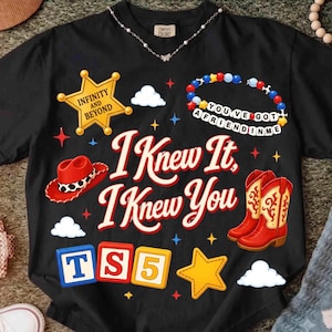 May include: A black t-shirt featuring the text I KNEW IT, I KNEW YOU in red. Graphics include a yellow sheriff badge with INFINITY AND BEYOND, a red cowboy hat, a beaded bracelet with YOU'VE GOT A FRIEND IN ME, red cowboy boots, and blocks with TS5.