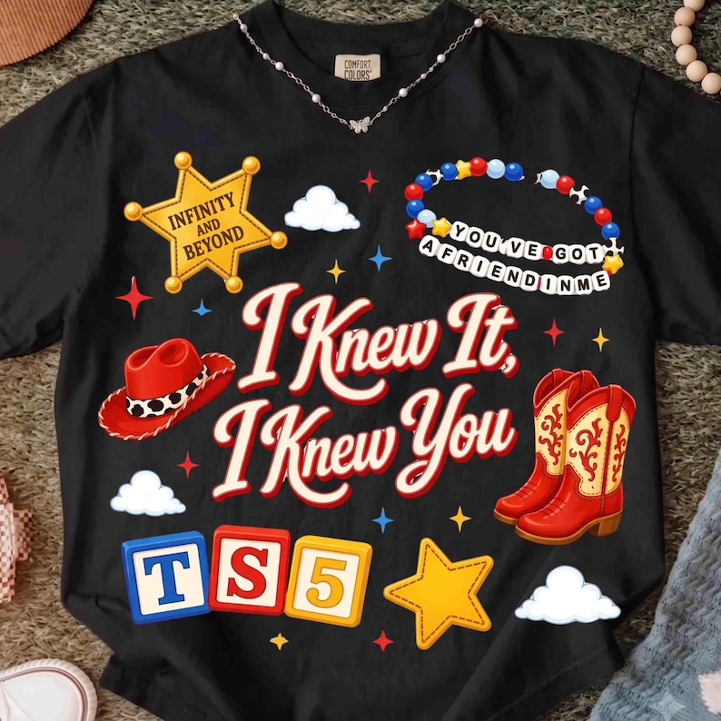 May include: A black t-shirt featuring the text I KNEW IT, I KNEW YOU in red. Graphics include a yellow sheriff badge with INFINITY AND BEYOND, a red cowboy hat, a beaded bracelet with YOU'VE GOT A FRIEND IN ME, red cowboy boots, and blocks with TS5.