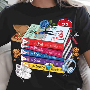 May include: Black t-shirt with a design featuring a stack of books by Elle Kennedy, including "The Deal" and "The Mistake". The design also includes a pizza box, cookies, trainers, a cocktail, and a hockey jersey.