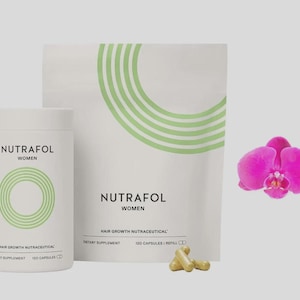 May include: A product shot features a white bottle and pouch of Nutrafol Women hair growth nutraceuticals, with a bright pink orchid and capsules. The bottle and pouch have green circular designs and text. The capsules are a light brown color.