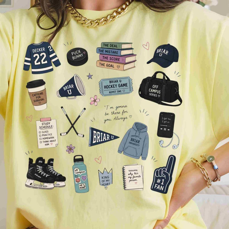 Puede incluir: Una camiseta amarilla clara con varias ilustraciones relacionadas con el hockey y la vida universitaria. Los dise&ntilde;os incluyen una camiseta de hockey, un disco, libros, una gorra de b&eacute;isbol, una bolsa de deporte y un smartphone con auriculares.