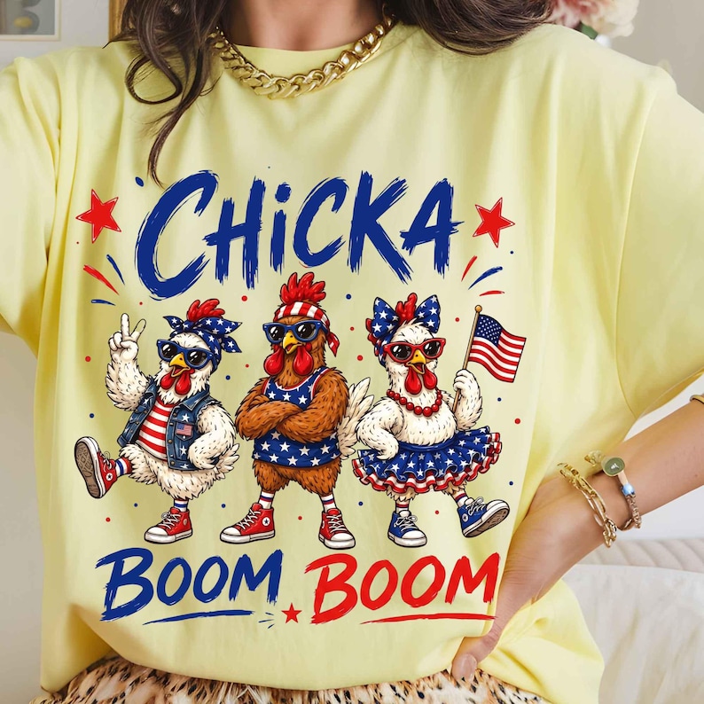 Puede incluir: Camiseta amarilla clara con un gr&aacute;fico de tres pollos vestidos con atuendos patri&oacute;ticos. Los pollos llevan gafas de sol, pa&ntilde;uelos y trajes con estrellas y rayas. El texto "Chicka Boom Boom" est&aacute; escrito encima y debajo de los pollos en azul y rojo.