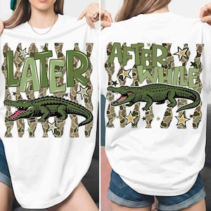 May include: White t-shirt featuring a green alligator graphic with the text "LATER" on the front and "AFTER WHILE" on the back. The design includes a camouflage pattern and star accents, creating a playful and casual look.