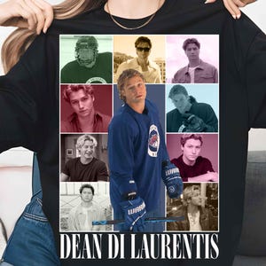 Puede incluir: Una camiseta negra con un collage de fotograf&iacute;as de una persona, incluyendo im&aacute;genes con equipo de hockey y ropa casual. La imagen central muestra a la persona con una camiseta de hockey azul sosteniendo un palo. El texto DEAN DI LAURENTIS est&aacute; impreso.