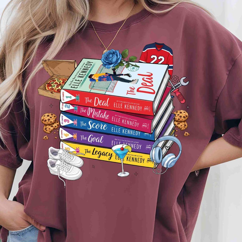 May include: A maroon t-shirt with a design featuring a stack of books titled "The Deal", "The Mistake", "The Score", "The Goal", and "The Legacy" by Elle Kennedy. The design includes a blue rose, pizza, cookies, trainers, a cocktail, and a hockey jersey.