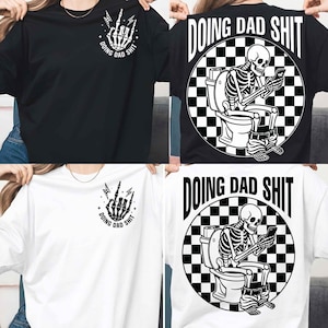 May include: Black and white t-shirts with the text "DOING DAD SHIT". One shirt features a skeleton hand with lightning bolts, and the other shows a skeleton on a toilet using a phone. Apparel.