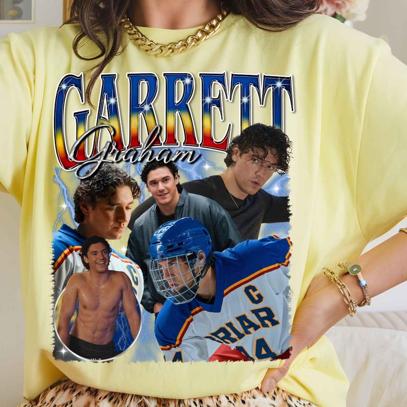 Puede incluir: Una camiseta de color amarillo p&aacute;lido con un estampado gr&aacute;fico que incluye el texto GARRETT Graham en una fuente azul y roja. El dise&ntilde;o muestra tres im&aacute;genes de un hombre, una de ellas sin camisa y otra con una camiseta de hockey azul y blanca.