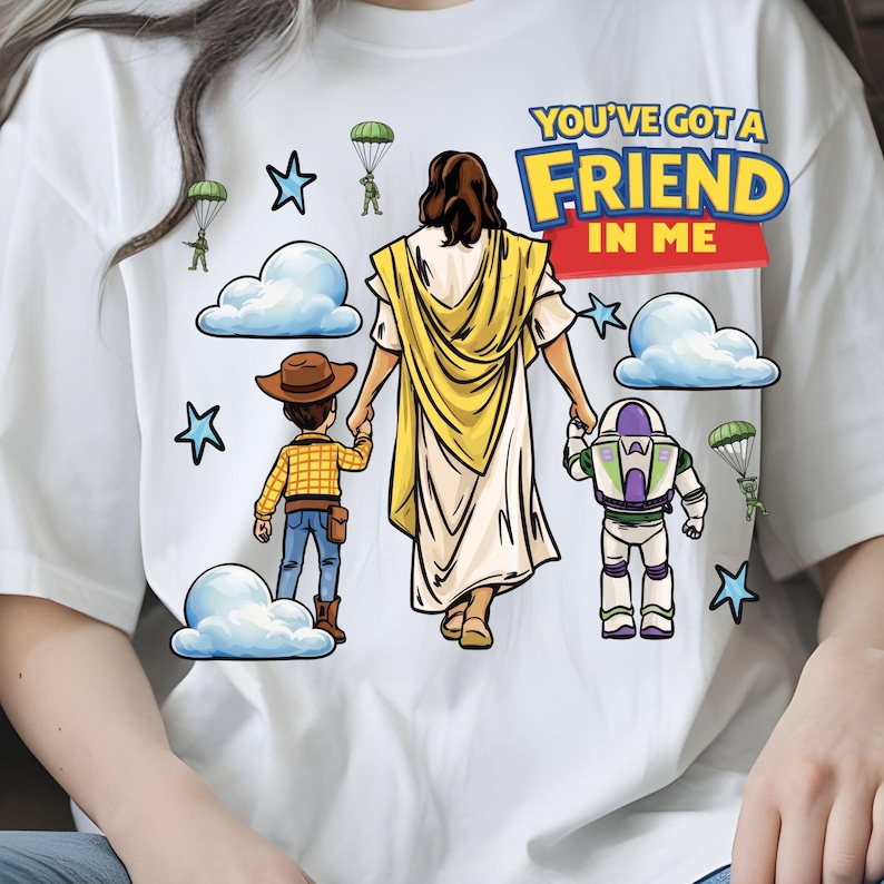 May include: White t-shirt featuring a graphic design with the text "YOU'VE GOT A FRIEND IN ME". The design includes cartoon illustrations of Jesus, Woody, and Buzz Lightyear, along with clouds, stars, and parachuting figures.