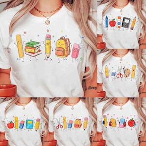 Könnte beinhalten: Ein weißes T-Shirt mit einem Grafikdruck von anthropomorphen Schulsachen, darunter ein gelbes Lineal, ein Bücherstapel, ein gelber Bleistift, ein orangefarbener Rucksack und ein rosa Radiergummi, alle mit lächelnden Gesichtern und dünnen schwarzen Gliedmaßen.
