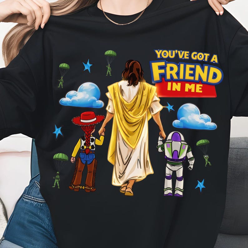 May include: Black t-shirt featuring a graphic of Jesus holding hands with cartoon characters. The text "YOU'VE GOT A FRIEND IN ME" is displayed in colorful letters above the figures. Blue stars, clouds, and parachuters are also included.