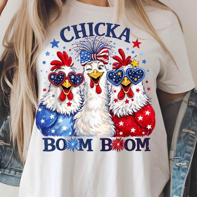 Puede incluir: Camiseta blanca con un dise&ntilde;o de tres pollos de dibujos animados con colores patri&oacute;ticos. Los pollos llevan gafas de sol en forma de coraz&oacute;n y tienen detalles en rojo, blanco y azul. El texto "CHICKA BOOM BOOM" est&aacute; impreso en azul.