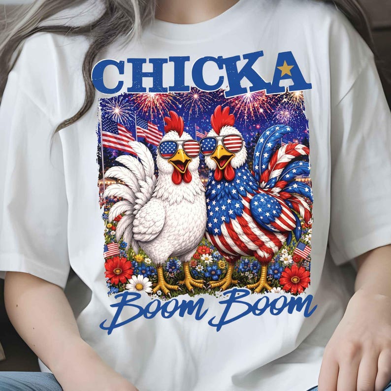 Puede incluir: Camiseta blanca con un gr&aacute;fico de dos gallos con gafas de sol con el dise&ntilde;o de la bandera estadounidense. La palabra "CHICKA" est&aacute; encima de los gallos, y "Boom Boom" est&aacute; escrito debajo. Fuegos artificiales y banderas americanas en el fondo.
