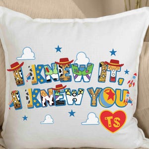 May include: A white square throw pillow featuring the text I KNEW IT, I KNEW YOU in blue and yellow block letters. The letters are filled with patterns of cowboy and space ranger character outfits. Includes blue stars, white clouds, rockets, and a red heart with TS.