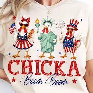 Puede incluir: Camiseta color crema con un dise&ntilde;o patri&oacute;tico con tres pollos de dibujos animados vestidos con atuendos de tem&aacute;tica americana. Los pollos sostienen un perrito caliente, una antorcha y fuegos artificiales. El texto "CHICKA Boom Boom" se muestra en rojo y azul.