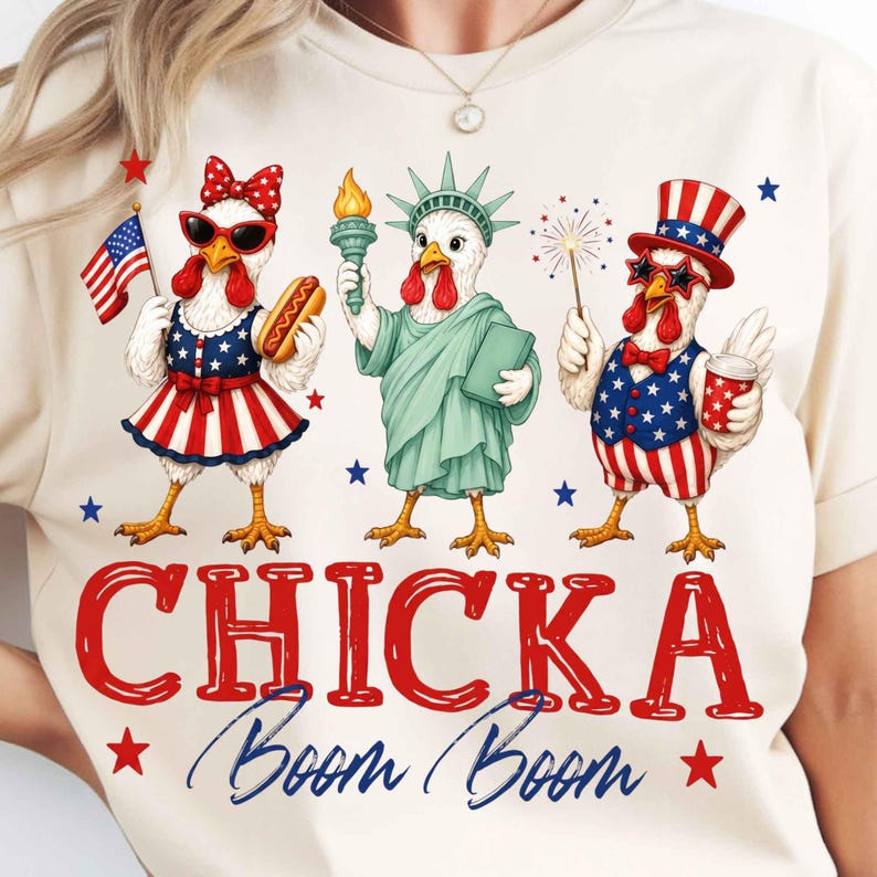 Puede incluir: Camiseta color crema con un dise&ntilde;o patri&oacute;tico con tres pollos de dibujos animados vestidos con atuendos de tem&aacute;tica americana. Los pollos sostienen un perrito caliente, una antorcha y fuegos artificiales. El texto "CHICKA Boom Boom" se muestra en rojo y azul.