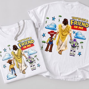 May include: Two white t-shirts with the phrase "YOU'VE GOT A FRIEND IN ME" printed on them. The shirts feature a graphic of a figure in a yellow robe holding hands with a cartoon cowboy and a space ranger. Blue clouds, stars, and parachutes are also included.