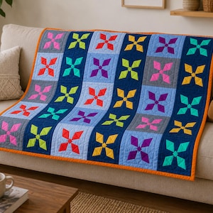 Könnte beinhalten: Eine rechteckige Steppdecke mit einem sich wiederholenden sternförmigen geometrischen Muster in leuchtenden Farben wie Pink, Limettengrün, Rot, Gelb, Violett und Türkis. Die Decke besteht aus abwechselnden hellblauen und dunkelblauen Bahnen mit einem orangefarbenen Rand.