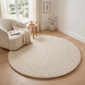 Peut inclure: Un grand tapis circulaire composé de nombreuses petites boules de laine feutrée de couleur crème, disposées en un motif en spirale concentrique, créant une surface texturée et sphérique sur tout le revêtement de sol rond.