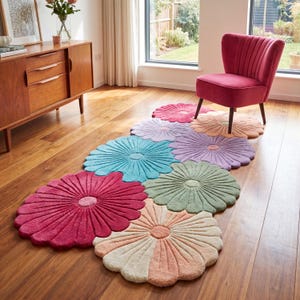 May include: A collection of colorful, flower-shaped rugs in shades of pink, blue, green, and purple. The rugs are arranged on a hardwood floor, with a red chair in the background. The rugs have a textured, petal-like design.