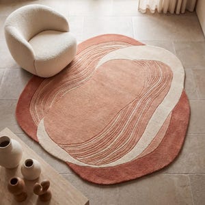 Könnte beinhalten: Runder Teppich mit abstraktem Design in Pfirsich-, Creme- und Terrakotta-Tönen. Der Teppich hat ein wellenförmiges Muster. Ein cremefarbener, abgerundeter Stuhl befindet sich in der Nähe des Teppichs.