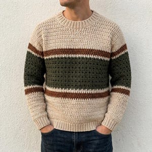 Könnte beinhalten: Ein langärmeliger Häkelpullover mit Rundhalsausschnitt und einem farblich abgesetzten Streifenmuster. Das Design besteht aus breiten cremefarbenen Bahnen, gefolgt von schmalen braunen Streifen und einem breiten Mittelstreifen aus dunkelolivgrünem Häkelmuster.