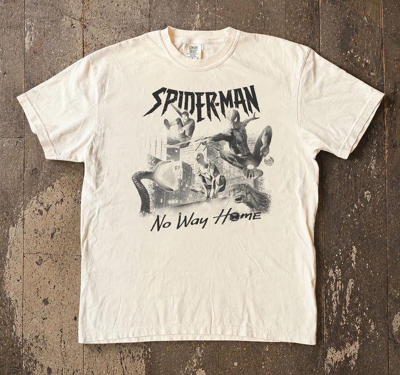 Może przedstawiać: Kremowa koszulka z czarno-białą grafiką Spider-Mana w akcji, z napisem "SPIDER-MAN" nad obrazem i "No Way Home" poniżej. Koszulka wykonana jest z miękkiego materiału.