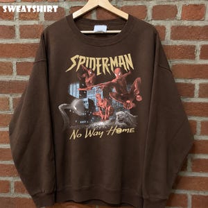 Może przedstawiać: Brązowa bluza z nadrukiem Spider-Mana w akcji, napisem "Spider-Man" i "No Way Home". Słowo "SWEATSHIRT" jest wydrukowane u g&oacute;ry.