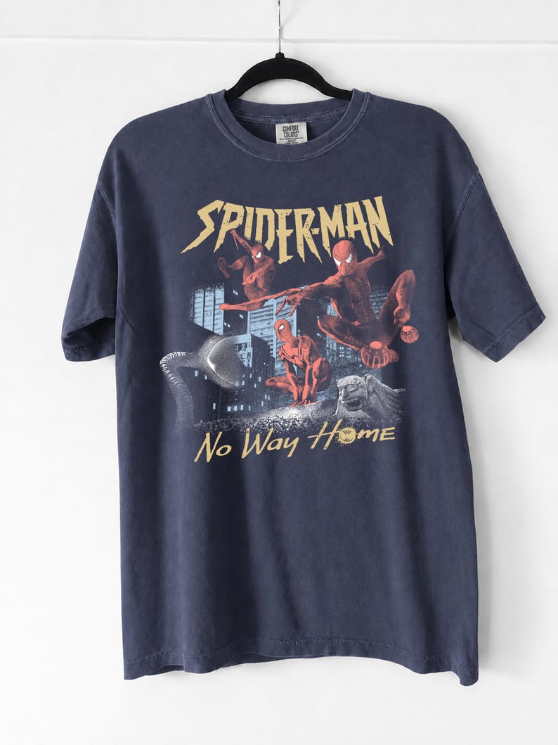 Może przedstawiać: Granatowa koszulka z nadrukiem Spider-Mana w akcji, złotymi napisami "SPIDERMAN" i "No Way Home", budynkami miejskimi i kamiennym gargulcem.