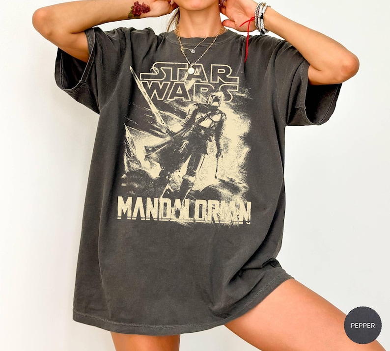 May include: Dark gray Star Wars Mandalorian graphic t-shirt. The shirt features the Star Wars logo and a graphic of the Mandalorian. The shirt is oversized with short sleeves.