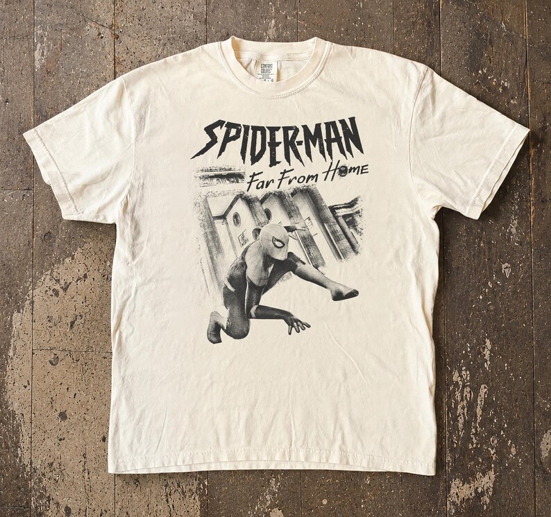 K&ouml;nnte beinhalten: Cremefarbenes T-Shirt mit einer Grafik von Spider-Man in dynamischer Pose und dem Text "SPIDERMAN Far From Home" in Schwarz. Das Design beinhaltet eine Graustufen-Illustration einer Stadtlandschaft. Das Shirt hat kurze &Auml;rmel und einen Rundhalsausschnitt.