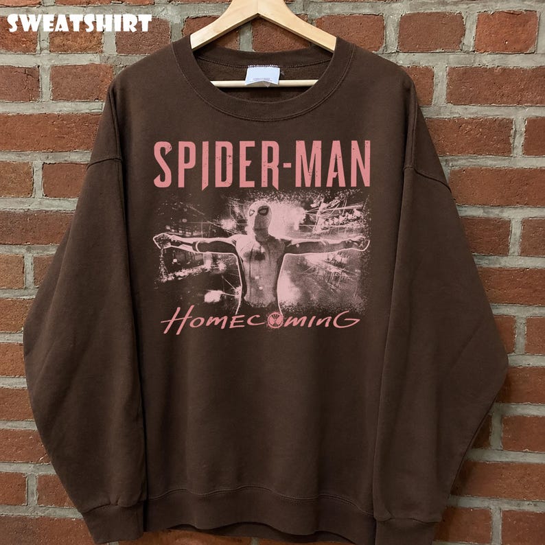 May include: Brown sweatshirt featuring the words "SPIDER-MAN" and "Homecoming" in pink lettering. The graphic depicts Spider-Man with outstretched arms. The word "SWEATSHIRT" is printed at the top of the image.