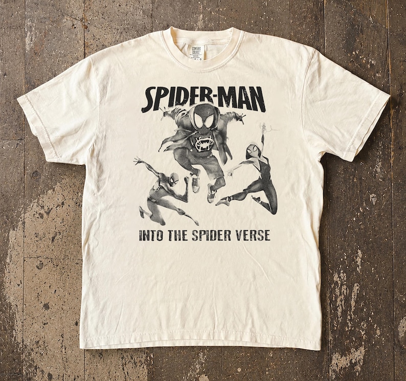 May include: Cream-colored t-shirt featuring a black and white graphic of Spider-Man and other Spider-Verse characters. The text "SPIDER-MAN" is above the graphic, and "INTO THE SPIDER VERSE" is below.