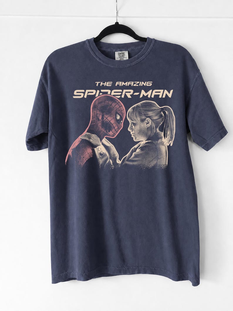 K&ouml;nnte beinhalten: Marineblaues T-Shirt mit einer Grafik von "The Amazing Spider-Man". Das Design zeigt Spider-Man und eine Frau, die sich gegen&uuml;berstehen. Der Text "THE AMAZING SPIDER-MAN" ist im Vintage-Stil &uuml;ber dem Bild gedruckt.