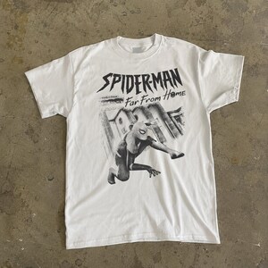 K&ouml;nnte beinhalten: Wei&szlig;es T-Shirt mit einer schwarz-grauen Grafik von Spider-Man aus dem Film "Far From Home". Das Design zeigt Spider-Man in einer dynamischen Pose vor einem Stadtbild. Der Text "SPIDERMAN Far From Home" ist &uuml;ber dem Bild gedruckt.