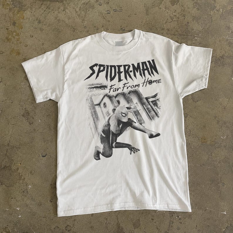 K&ouml;nnte beinhalten: Wei&szlig;es T-Shirt mit einer schwarz-grauen Grafik von Spider-Man aus dem Film "Far From Home". Das Design zeigt Spider-Man in einer dynamischen Pose vor einem Stadtbild. Der Text "SPIDERMAN Far From Home" ist &uuml;ber dem Bild gedruckt.