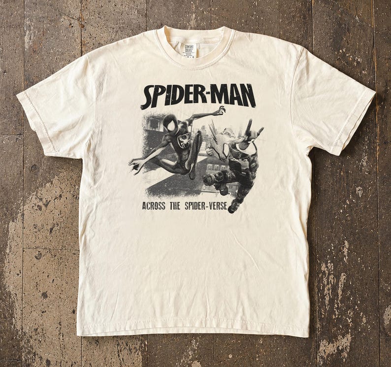 Puede incluir: Camiseta color crema con un dise&ntilde;o en blanco y negro de Spider-Man en acci&oacute;n. El texto "SPIDER-MAN" est&aacute; sobre la imagen y "ACROSS THE SPIDER-VERSE" debajo. Cuello redondo y mangas cortas.