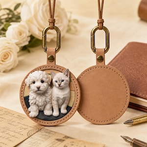 Può includere: Un portachiavi rotondo in pelle color cuoio con un rilievo 3D dettagliato di un cucciolo bianco soffice e un gattino chiaro. Il portachiavi presenta una chiusura in metallo color bronzo e un cordino marrone, con il retro in pelle liscia.