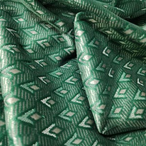 May include: A deep green fabric featuring a repeating geometric pattern of small silver diamonds and chevron lines. The material has a subtle sheen and is folded to show the texture and the intricate woven design across the surface of the textile.