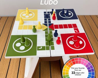 May include: A Ludo board game titled PLAYBOOK'D LUDO with yellow, green, red, and blue sections, matching coloured game pieces, and a brown die. A circular colour wheel graphic displays the text: Pick your favourite from our 33 unique colour choices!