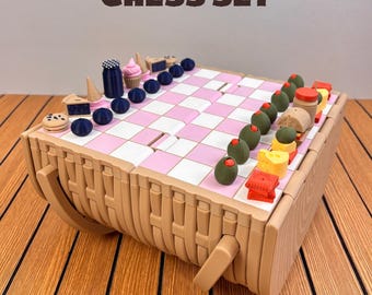 May include: A picnic chess set with a pink and white chequered board atop a tan woven-style basket base. The game pieces are shaped like food items, including blueberries, cupcakes, olives, cheese, and crackers. Text reads PICNIC CHESS SET.