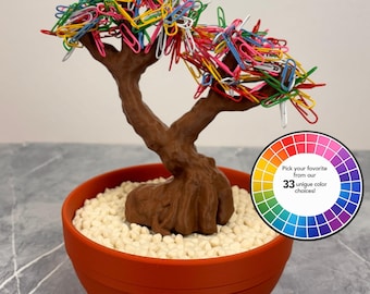 May include: A brown tree-shaped sculpture with branches covered in multi-coloured paper clips, set in a round orange pot filled with small white pebbles. A circular graphic displays a colour wheel with the text Pick your favourite from our 33 unique colour choices!