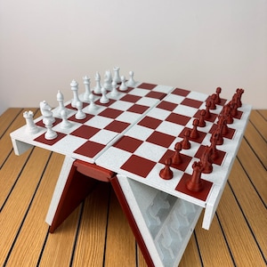 K&ouml;nnte beinhalten: Ein klappbares Schachspiel mit einer wei&szlig;-roten Schachbrettoberfl&auml;che. Eine Seite enth&auml;lt wei&szlig;e Schachfiguren, w&auml;hrend die andere Seite dunkelrote Figuren enth&auml;lt. Das Brett wird von einem V-f&ouml;rmigen Sockel mit internen F&auml;chern gest&uuml;tzt.