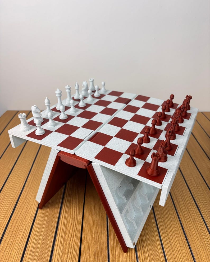 K&ouml;nnte beinhalten: Ein klappbares Schachspiel mit einer wei&szlig;-roten Schachbrettoberfl&auml;che. Eine Seite enth&auml;lt wei&szlig;e Schachfiguren, w&auml;hrend die andere Seite dunkelrote Figuren enth&auml;lt. Das Brett wird von einem V-f&ouml;rmigen Sockel mit internen F&auml;chern gest&uuml;tzt.