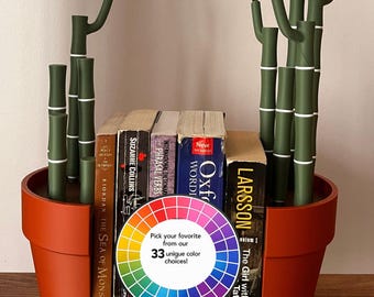 May include: Two terracotta-coloured bookends shaped like bamboo stalks in pots, holding a row of books. A circular colour wheel graphic is placed in the centre with the text: Pick your favourite from our 33 unique colour choices!