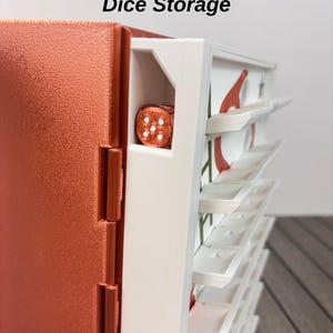 May include: A copper-colored dice storage case with a white side panel featuring multiple horizontal slots. The text Dice Storage is printed at the top. A single copper die with white pips is visible in the top slot of the white section.