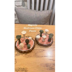 K&ouml;nnte beinhalten: Zwei Sets von Pilz-Schachfiguren auf Holzsockeln. Die Sockel sind braun mit roten und wei&szlig;en konzentrischen Kreisen. Die Schachfiguren sind in verschiedenen Farben gehalten, darunter Wei&szlig;, Gr&uuml;n und Braun. Der Text "Magnetic Mushroom Chess Pieces" ist sichtbar.